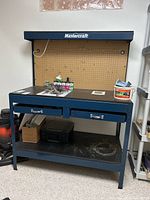 Front view of Mastercraft metal workbench with pegboard, light on top, two drawers, and items on top and bottom shelf.