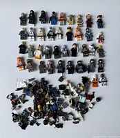 Top down view showing about 40 fully assembled LEGO minifigs arranged at top with a pile of loose parts and weapons at bottom.