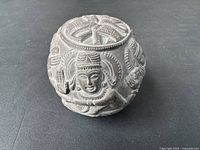 Side view of the hand-carved stone sphere showing a detailed carved Indian deity face and ornate patterns.