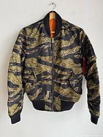 Front view of reversible bomber jacket featuring camouflage design with ribbed collar, cuffs, and hem in black.