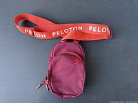 Peloton waist bag fanny pack with front and main compartment visible and red strap with Peloton text.