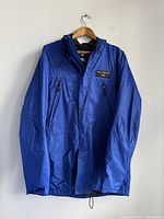 Front view of a blue lightweight vintage jacket with zipper pockets and hood on a hanger.
