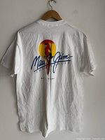 Back side of the white Maui Jim T-shirt showing a large colorful parrot graphic with sun and 'Maui Jim Sunglasses' text and Maui Hawaii text below.