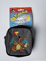Front of card holder with embroidered Charizard on grey fabric, original packaging backing in background.