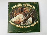 Front cover of Richie Havens Somethin' Else Again vinyl record album showing artist playing sitar with green background and yellow title text.