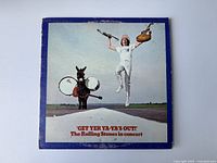 Front cover of The Rolling Stones vinyl album 'Get Yer Ya-Ya's Out!' showing person jumping and donkey playing drums on open road.