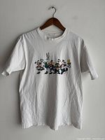 White T-shirt front view showing Looney Tunes characters lined up with a soccer ball, hanging on a hanger.