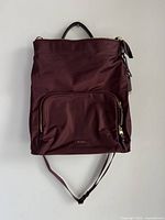 Front view of the burgundy convertible backpack with a front zipper pocket and the Tumi logo visible.