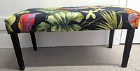Side view of bench showing cushioned seat covered with bird and leaf print fabric and black wooden legs.