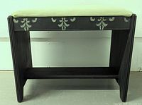 Front angled view showing stool's black frame, floral stencil decoration on apron, and light green padded seat