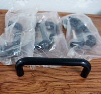 Close-up of black plastic drawer pulls, one removed from packaging showing shape and size