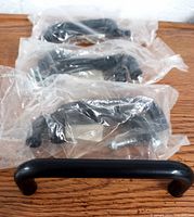 Photo of six black plastic drawer pulls, all individually packaged in clear plastic with mounting screws visible.