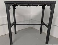 Front view of the black wooden side table showing carved leg details and edge trim.