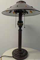 Bronze table lamp showing full length, ribbed column design, and metal shade with colored faux stones around the edge.