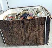 Large cardboard box with a wood grain printed exterior, filled with costume jewelry items and accessories.