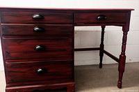 Front side view of wooden desk showing four drawers with modern black metal pulls and the painted black and red finish.