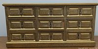 Front view of golden wood jewelry box with 7 drawers closed, showing decorative handles and panels.