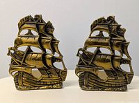 Front view of the pair of brass ship bookends showing detailed sailing ship design.