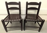 Front view of two dark brown wooden children's chairs placed side by side, showing the ladder-style backrests and slatted seats.