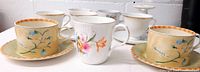 Photo of front view of teacups and saucers showing Royal Stafford two cup and saucer sets with floral design and Sadler Wellington mug among other cups