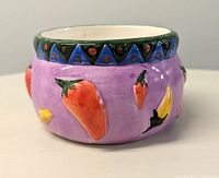 Close-up photo of a single ceramic salsa bowl showing the purple exterior with red, orange, and yellow chili pepper decorations and blue patterned rim.