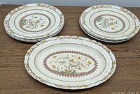 Six 9-inch dinner plates and one 11-inch oval serving dish arranged on a wooden table, showing the detailed floral Buttercup pattern and scalloped edges.
