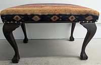 Side view of the wooden bench showing ball and claw legs and upholstery with nailhead accents.