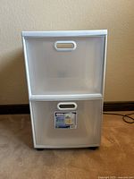 Front view of white plastic 2-drawer storage cart with translucent pullout bins and label on lower drawer.