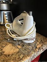 White KitchenAid handheld electric mixer with cord wrapped around, two metal beaters attached, placed on a granite countertop.