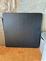 Square black folding table surface leaning against wall