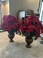 Pair of large faux red poinsettias in matching bronze-tone urn-shaped vases displayed on floor in living room