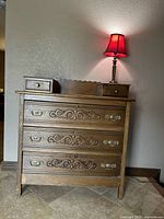 Front view of the antique wooden chest of drawers showing detail in carved motifs and metal pulls.