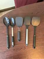 Set of five black cooking utensils laid side by side on a wooden surface.