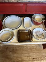 Top view of drawer showing all bowls and dishes stacked and nested including white mixing bowls, red and cream nested bowls, rectangular baking dishes, glass baking dish, and decorative bowl.