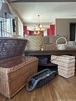 View of assortment of different shaped and colored baskets including a large rectangular basket chest and smaller baskets stacked and arranged inside and outside of wooden furniture.
