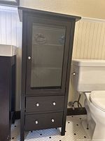 Full view of dark wood bathroom cabinet with glass door and two drawers below, positioned beside a toilet and vanity.