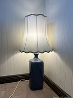 Full view of the blue ceramic table lamp with white scalloped fabric shade turned on, showing overall shape and size.