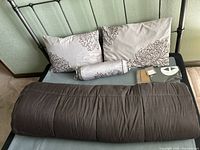 Overview of queen bedding set with brown comforter, two floral decorative pillows, lumbar pillow, and two pillowcases on bed frame.