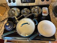 Overview of cookware on stove, showing variety of pots and pans with lids including frying pan and ceramic pot