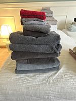 Stacked towels of various colors and sizes including bath towels, hand towels, and washcloths shown on a bed with white quilt.