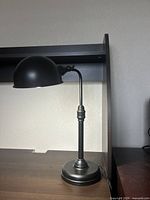 Black metal adjustable desk lamp with rounded shade and rotary switch on neck.