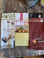 Eight assorted dish and hand towels neatly folded in two columns, showing a mix of seasonal and everyday prints and colors.