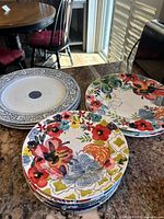 Stack of ceramic dinner plates with colorful floral patterns and black and white design plates, showing details of floral motifs and color palettes.