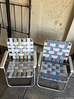Pair of colorful folding lawn chairs with metal frames and woven plastic straps in a garage setting.