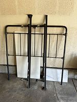 Full size black metal bed frame and headboard leaning against a wall in garage.