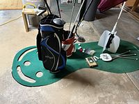 Wide view of two golf bags filled with clubs positioned on a green smiling face putting mat, with golf balls, tees and training tools laid out