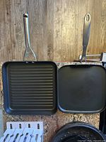 Photo of two square non-stick griddle pans; one ridged and one flat, both with metal handles.