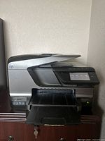 Full view of HP Officejet Pro printer with paper output tray extended and power light on, positioned on wooden surface.
