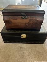 Two stacked jewelry boxes: a dark wood box with decorative latch sitting atop a black box with gold trim and latch