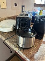 Overview photo showing from left to right: white panini press, black two-slot toaster, black electric can opener, and a stainless steel Crock-Pot Mini slow cooker on a kitchen counter.